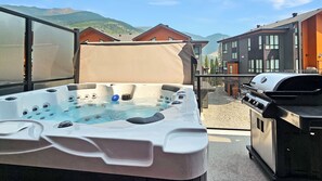 Ein Whirlpool mit Blick auf Berge, ein Grill und moderne Gebäude im Hintergrund.