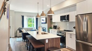 Una cocina moderna con una isla central, electrodomésticos de acero inoxidable, iluminación colgante y vistas al exterior.