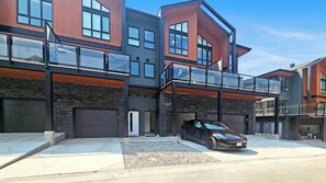 Un edificio residencial moderno de varios pisos, con un garaje, un área exterior cubierta y un coche estacionado al frente.
