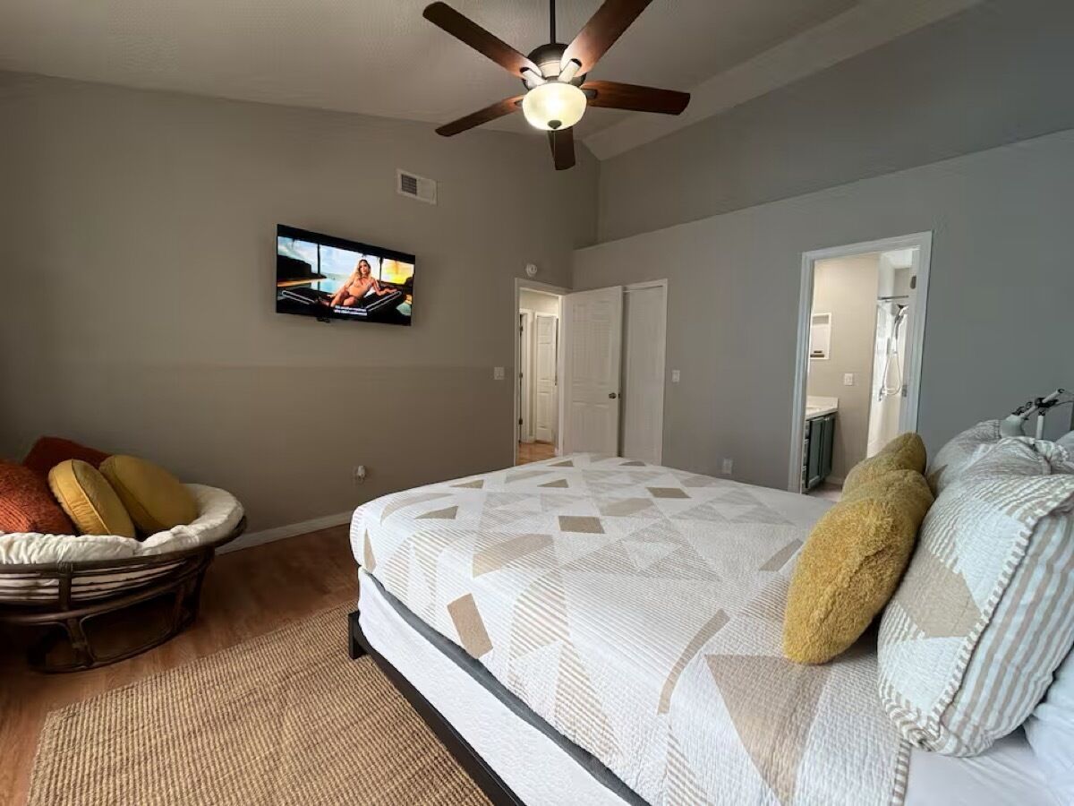 Une chambre à coucher avec un lit, un téléviseur, un ventilateur de plafond et une porte.