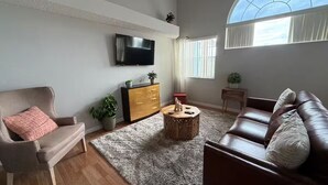A living room with a flat-screen TV mounted on the wall, a brown leather sofa, a wooden coffee table, and a grey shaggy rug. - Lyrios Vacation Rentals - The Villas (Kissimmee)