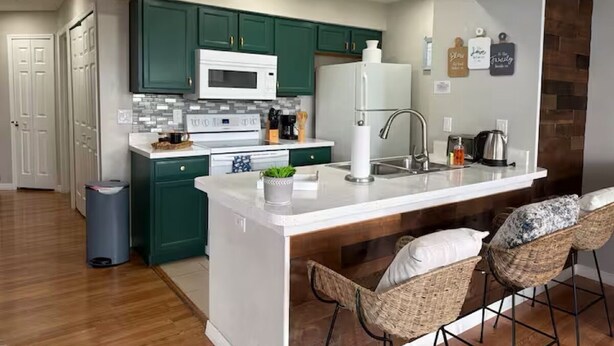 A modern kitchen with green cabinets, a white countertop, and a central island with bar stools. - Lyrios Vacation Rentals - The Villas (Kissimmee)