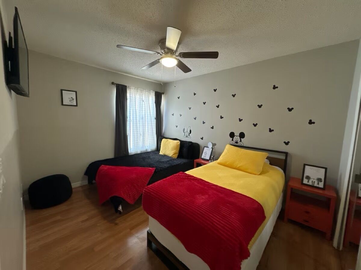 A bedroom with two beds, a ceiling fan, a nightstand, and a window with curtains.