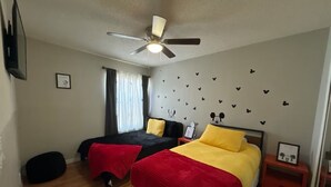 A bedroom with two beds, a ceiling fan, a nightstand, and a window with curtains. - Lyrios Vacation Rentals - The Villas (Kissimmee)