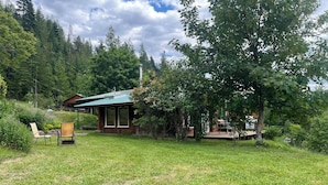A wooden cabin with a green roof, surrounded by lush greenery and trees.