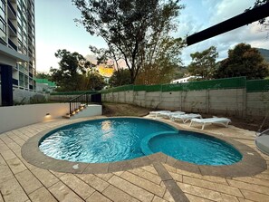 A swimming pool with a curved design, surrounded by a tiled deck and a low wall. - Cozy 1 bedroom apartment with AC in San Salvador (San Salvador)