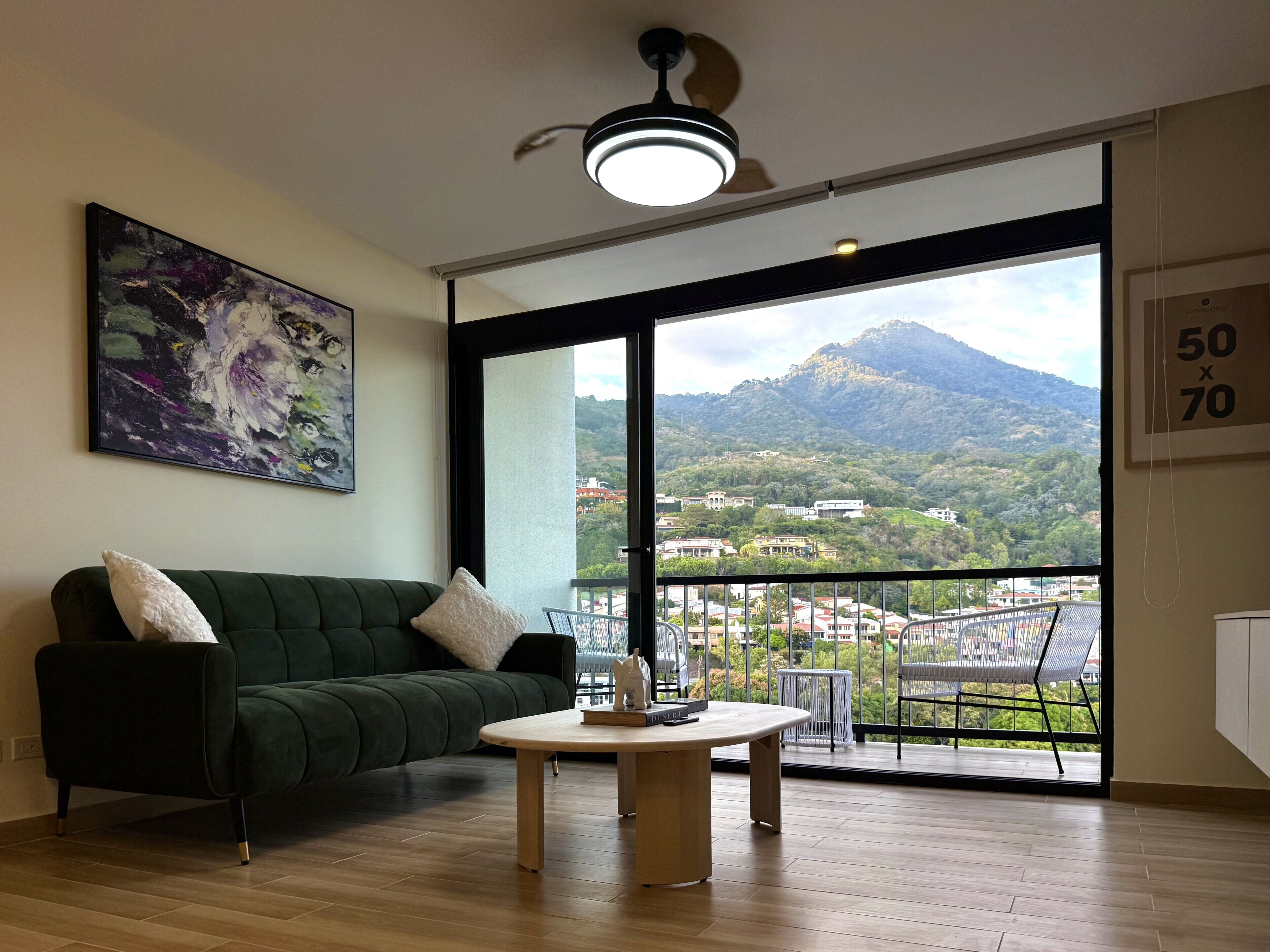 Un salon moderne avec un canapé vert, une table basse ronde en bois et une grande fenêtre donnant sur une vue imprenable sur les montagnes.