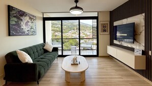 A modern living room with a sofa, a coffee table, a TV, and a large window with a city view. - Cozy 1 bedroom apartment with AC in San Salvador (San Salvador)