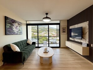 A modern living room with a sofa, a coffee table, a TV, and a large window with a city view. - Cozy 1 bedroom apartment with AC in San Salvador (San Salvador)
