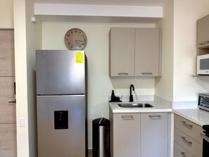 A kitchen with a stainless steel refrigerator, a microwave, a sink with a faucet, and a clock on the wall. - Cozy 1 bedroom apartment with AC in San Salvador (San Salvador)