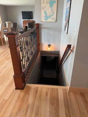 Un escalier en bois, doté d’une rampe métallique, mène à un palier. Un téléviseur à écran plat est fixé au mur, au-dessus du palier.