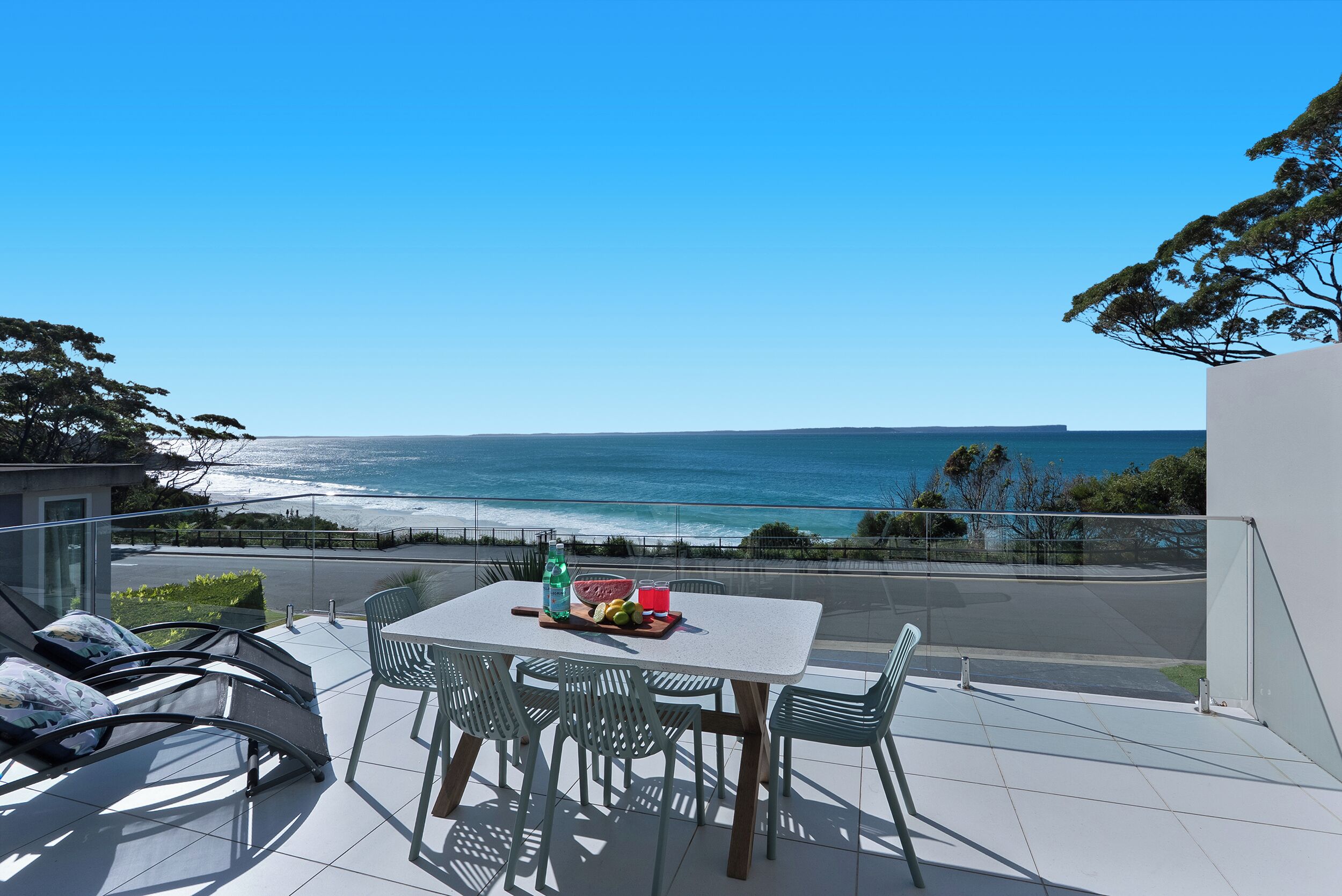 Een balkon met tafel en stoelen met uitzicht op de oceaan.