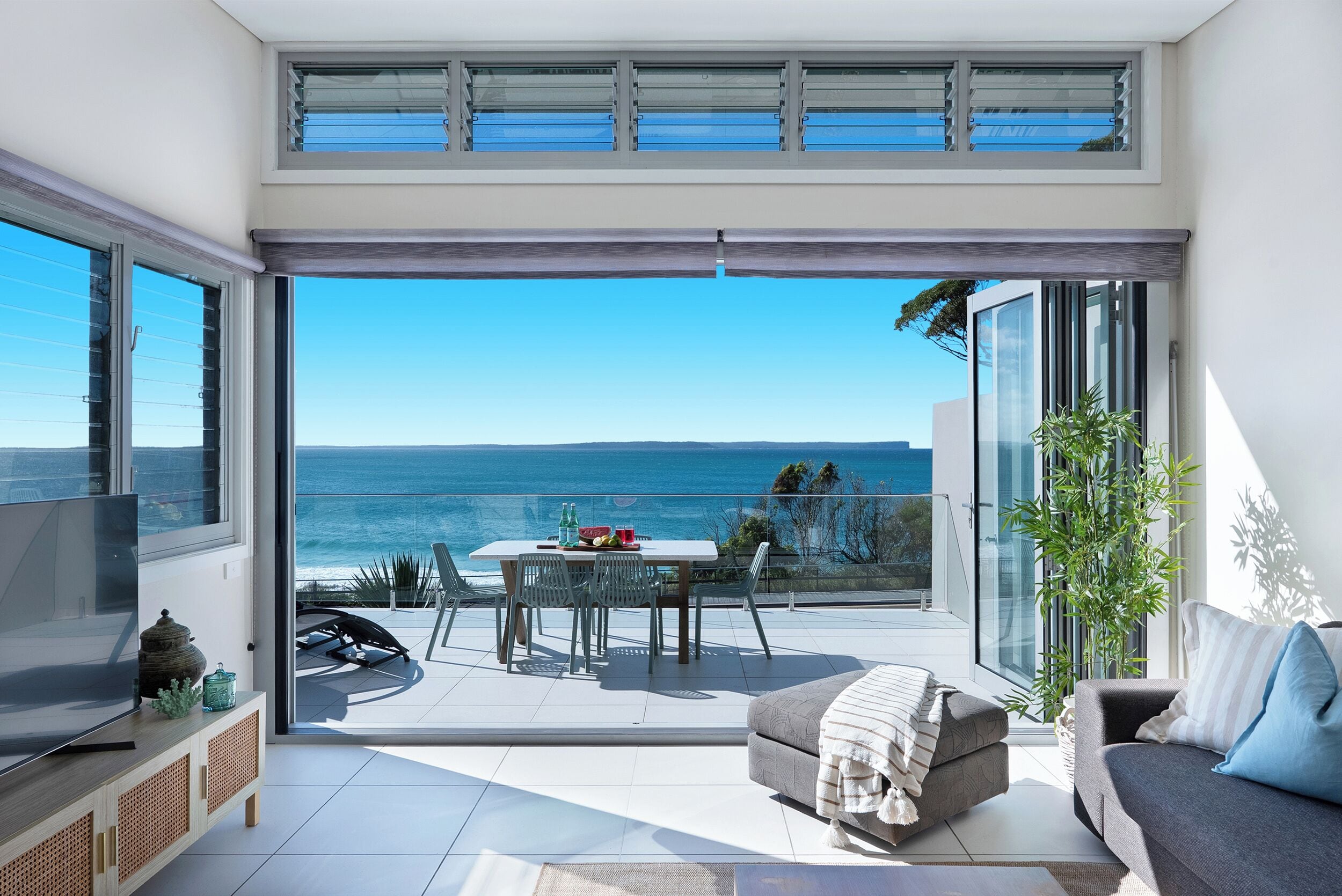 A modern living room with a large sliding glass door leading to a balcony with a view of the sea.