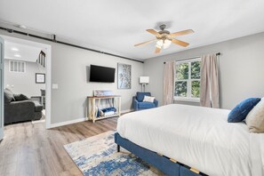 A modern bedroom with a large bed, a ceiling fan, a TV, and a window with curtains.