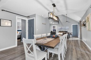 A modern dining area with a wooden table, white chairs, and pendant lighting.