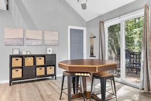 Un comedor con una mesa de madera, taburetes de bar, un mueble negro con cestas y vistas al exterior a través de un ventanal corredero.