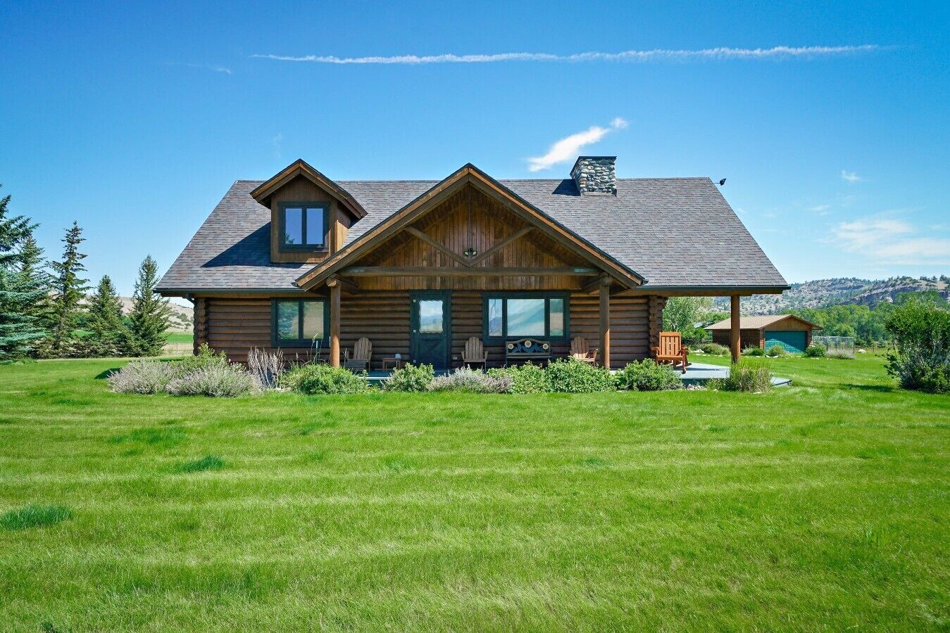 A log cabin with a large porch, multiple windows, and a stone chimney.