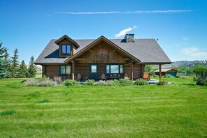 A log cabin with a large porch, multiple windows, and a stone chimney.