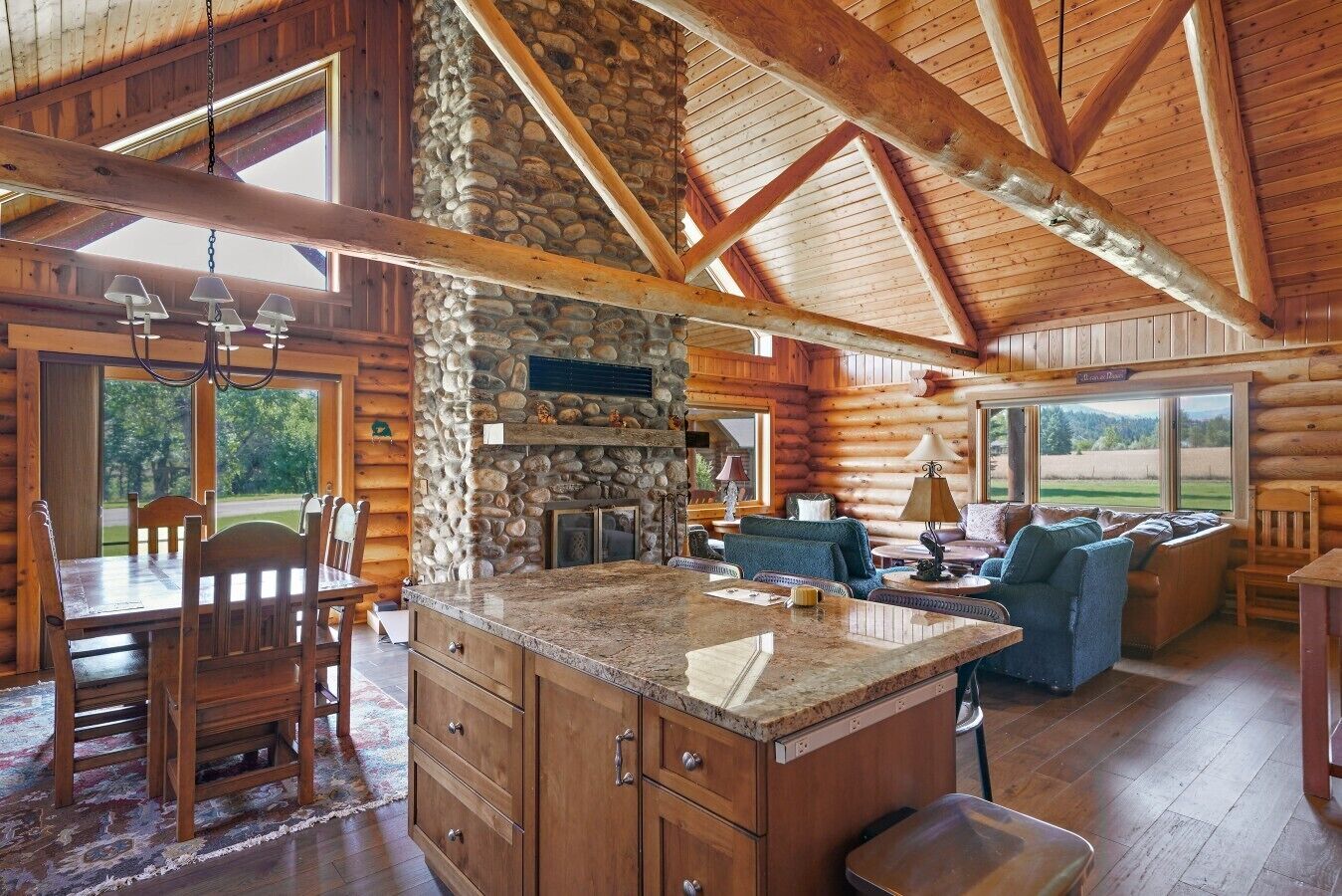 A log cabin interior with a stone fireplace, wooden dining area, and a cozy living space.