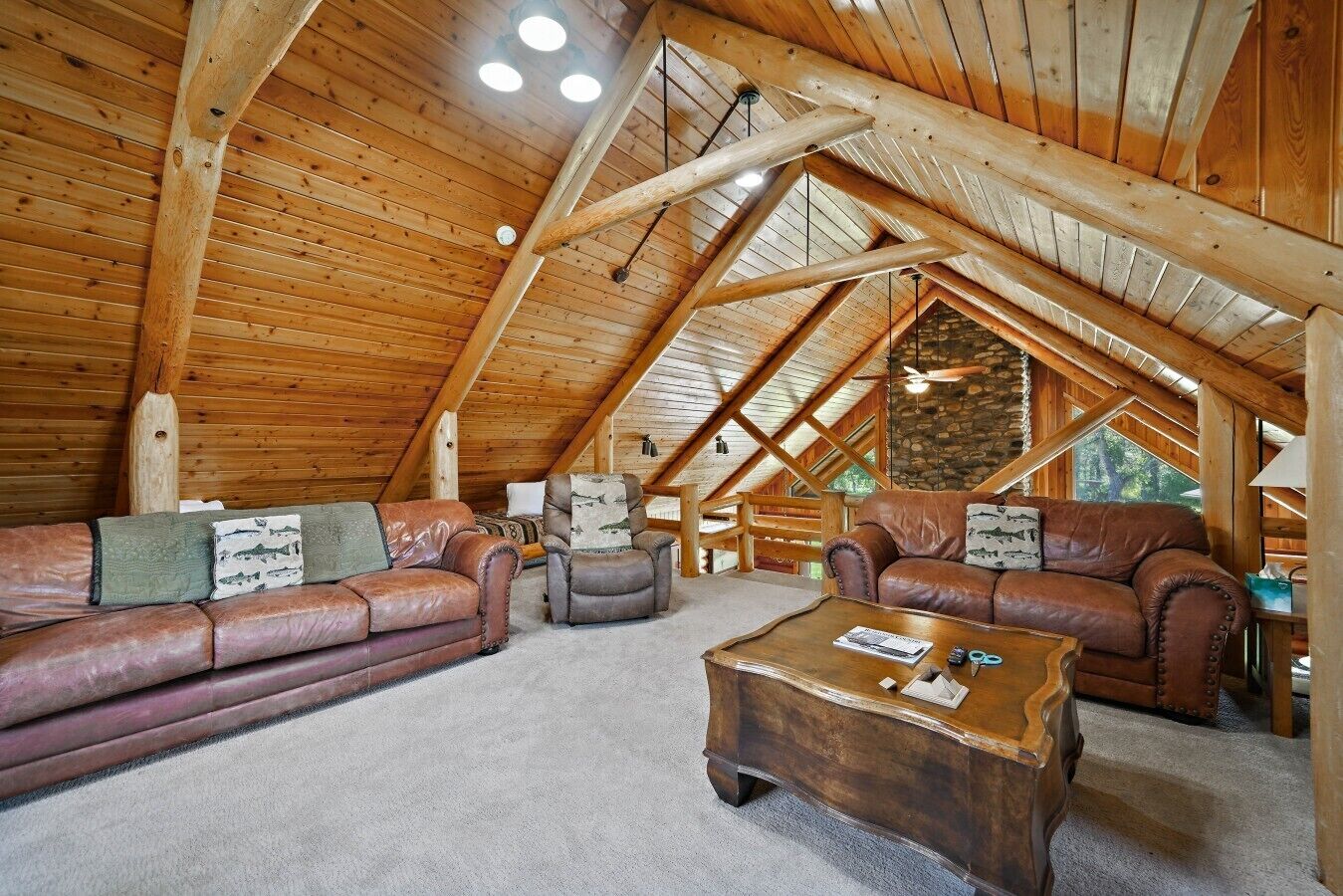 Ein rustikales Holzblockhaus-Interieur mit hohen Decken, Holzbalken, Ledersofas und einem Kamin aus Stein.