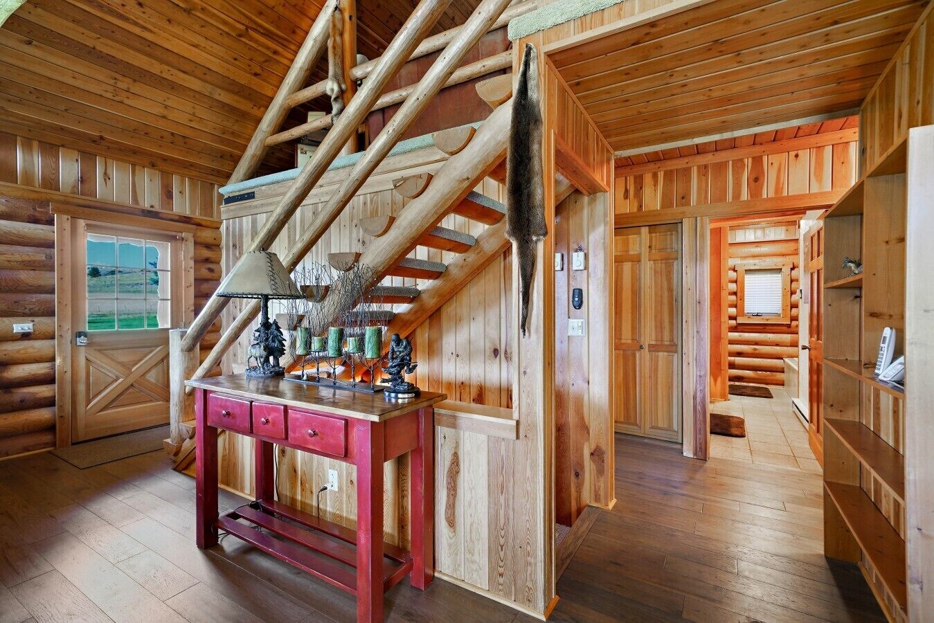 A wooden interior with a staircase, a desk with drawers, and a door leading outside.