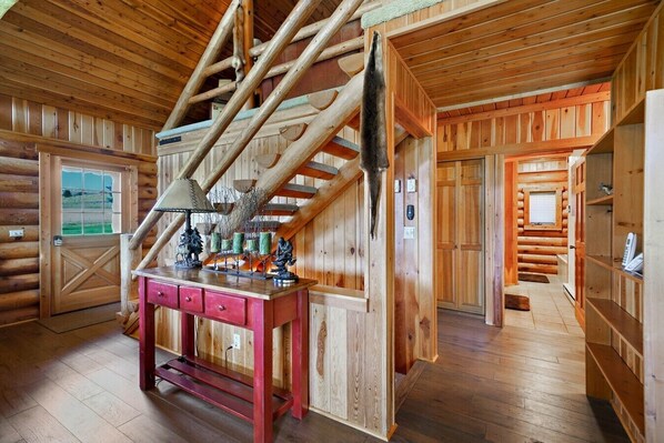A wooden interior with a staircase, a desk with drawers, and a door leading outside.