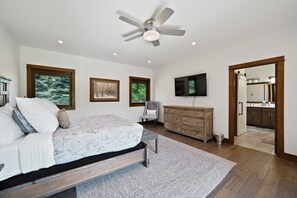 A bedroom with a bed, a dresser, a television, and a door leading to a bathroom.