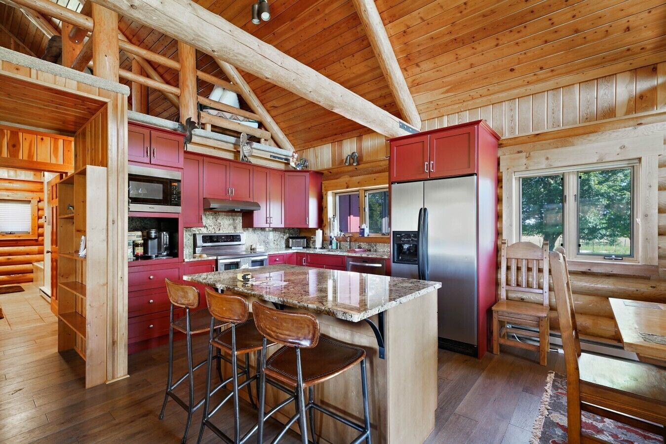 Cocina de cabaña de madera con una isla central, armarios rojos, electrodomésticos de acero inoxidable y techo de madera.