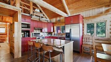 Cocina de cabaña de madera con una isla central, armarios rojos, electrodomésticos de acero inoxidable y techo de madera.