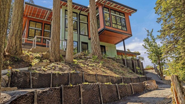 Uma casa moderna de dois andares com telhado inclinado, janelas amplas e um muro de arrimo de pedra.