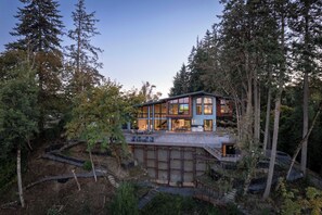 Ein modernes, zweistöckiges Haus mit einer großen Glasfassade, umgeben von dichtem Wald.