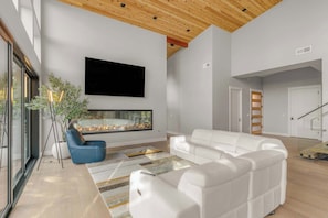 Ein modernes Wohnzimmer mit Kamin, weißen Sofas, einem blauen Sessel und einem großen Fernseher.