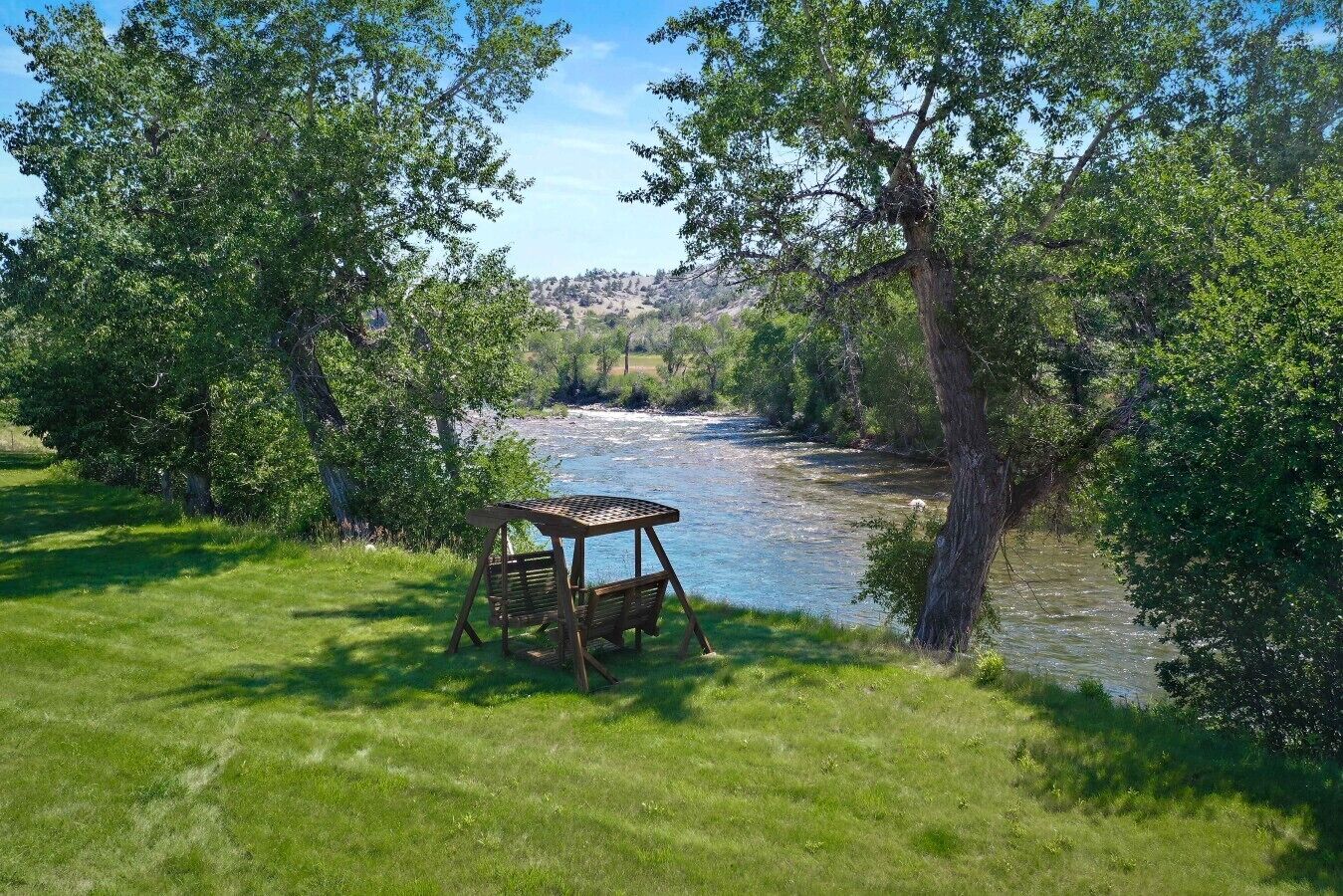 Uitzicht op een rivier met een houten prieel en weelderige begroeiing.