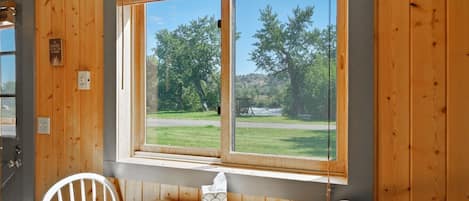 Una habitación con un ventanal grande, paredes de madera, una mesa con sillas y vista a un área verde con árboles.
