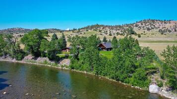 A riverside property with a cabin and a larger building, surrounded by trees and hills.