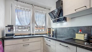 Una cocina moderna con microondas integrado, cafetera y lavamanos. Hay armarios con manijas y una ventana con cortinas.