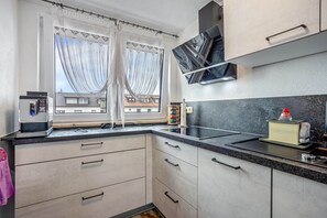 Una cocina moderna con microondas integrado, cafetera y lavamanos. Hay armarios con manijas y una ventana con cortinas.
