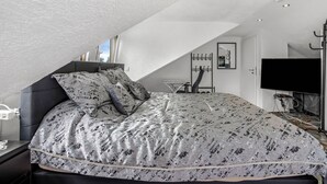 Un dormitorio con techo inclinado, una cama con ropa de cama estampada, un televisor y un perchero.