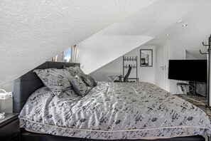Un dormitorio con techo inclinado, una cama con ropa de cama estampada, un televisor y un perchero.