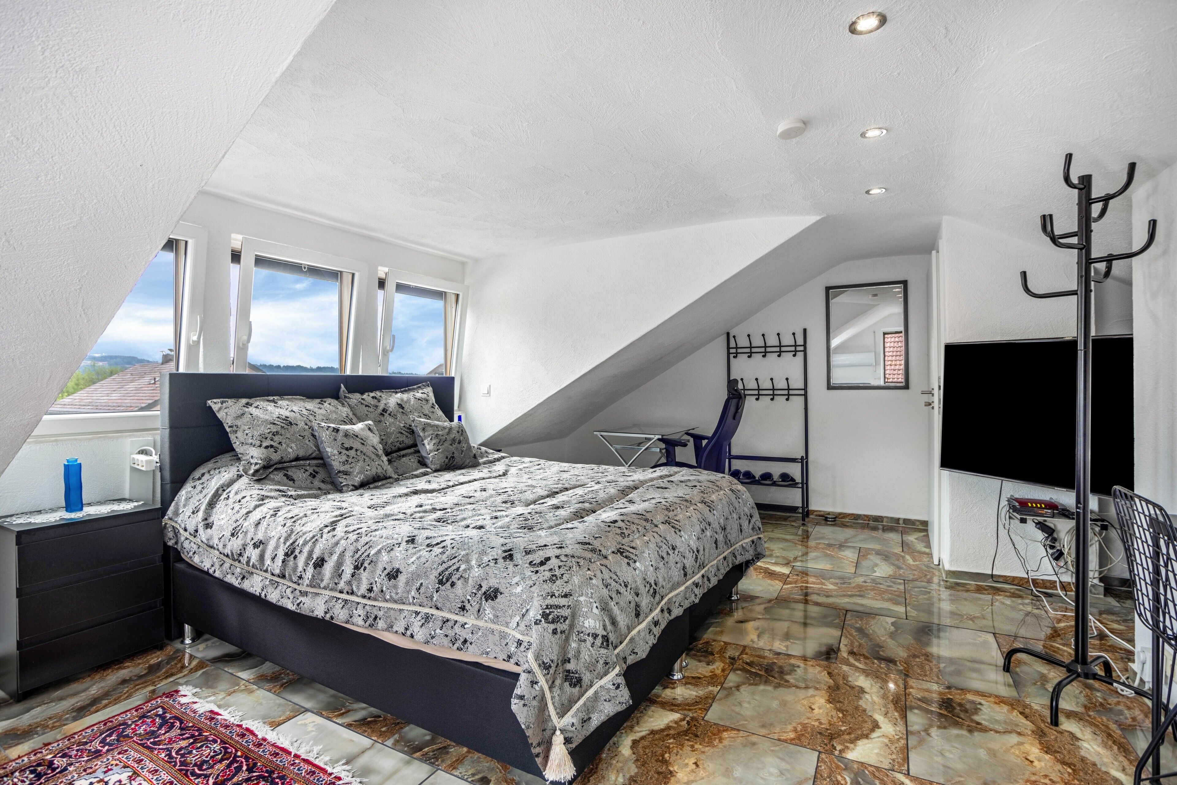 Ein Schlafzimmer mit einem Bett, einem Fernseher, einem Kleiderständer und einem Fenster.