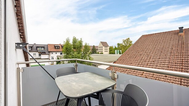 Un balcón con mesa y sillas, con vista a una zona residencial con casas y árboles.