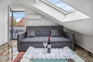 A modern loft bedroom with a grey sofa, a glass coffee table, and a bottle of wine.