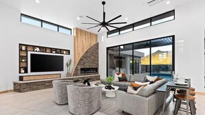 A modern living room with a large TV, a fireplace, a sofa, and a dining area. - Luxury Mansion w/ Private Pool & Spa l Mini Golf (Hurricane)