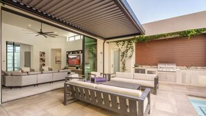 A modern outdoor living area with a sofa, a dining table, and a grill. - Luxury Mansion w/ Private Pool & Spa l Mini Golf (Hurricane)