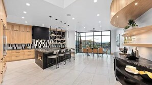 A modern kitchen with a central island, bar stools, and a dining area with chairs. - Luxury Mansion w/ Private Pool & Spa l Mini Golf (Hurricane)