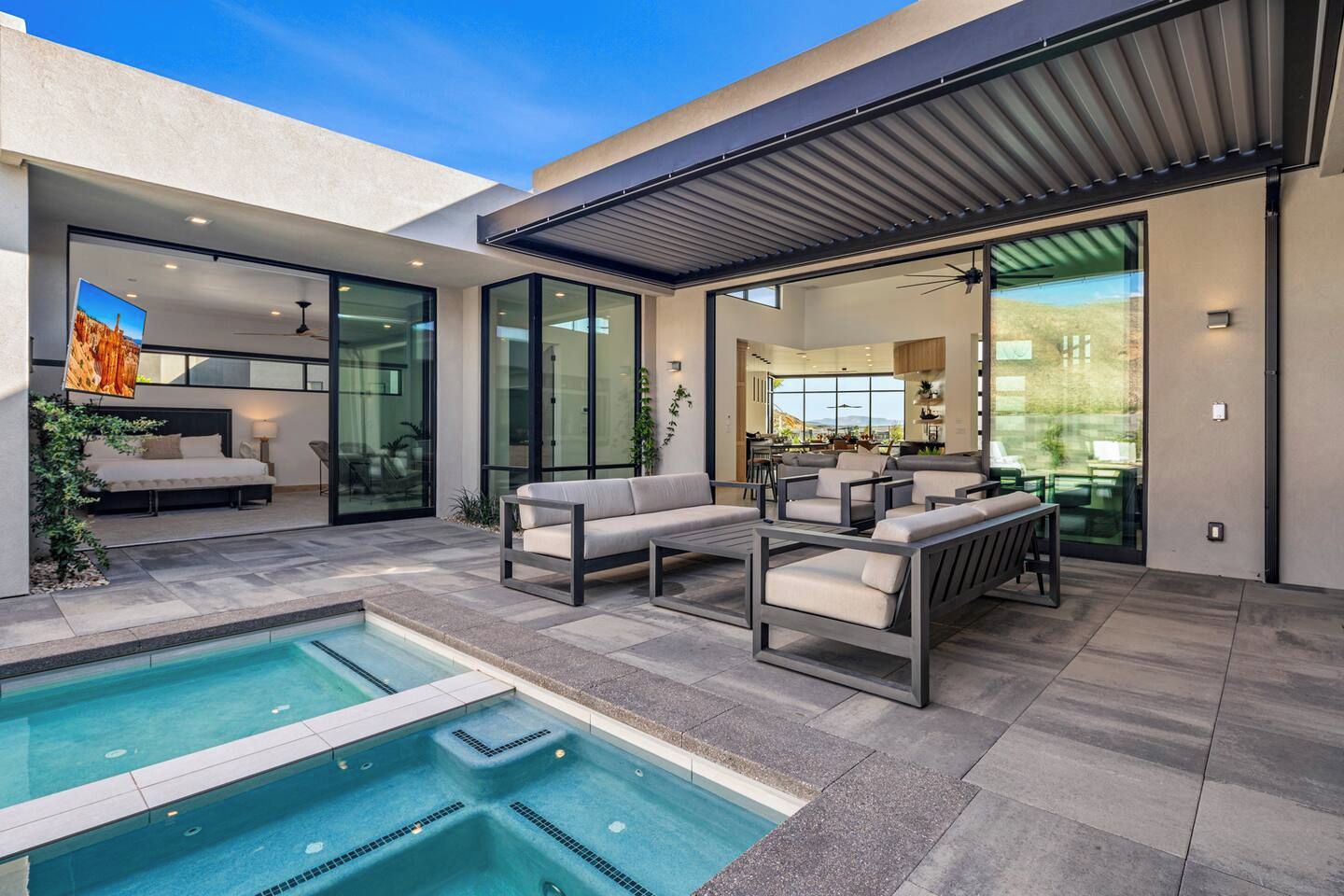 A modern outdoor living area with a pool, seating, and a glass-enclosed dining space.