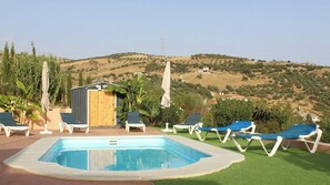A swimming pool with lounge chairs, a small shed, and a view of a hilly landscape. - Casa Rural de Piedra Valle de Abdalajís by Ruralidays (Málaga)