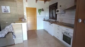 A kitchen with white cabinets, a microwave, and a stove. There is a door leading to another room. - Casa Rural de Piedra Valle de Abdalajís by Ruralidays (Málaga)