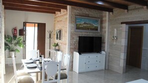 A dining area with a brick wall, a flat-screen TV mounted above a white cabinet, and a dining table set with chairs. - Casa Rural de Piedra Valle de Abdalajís by Ruralidays (Málaga)