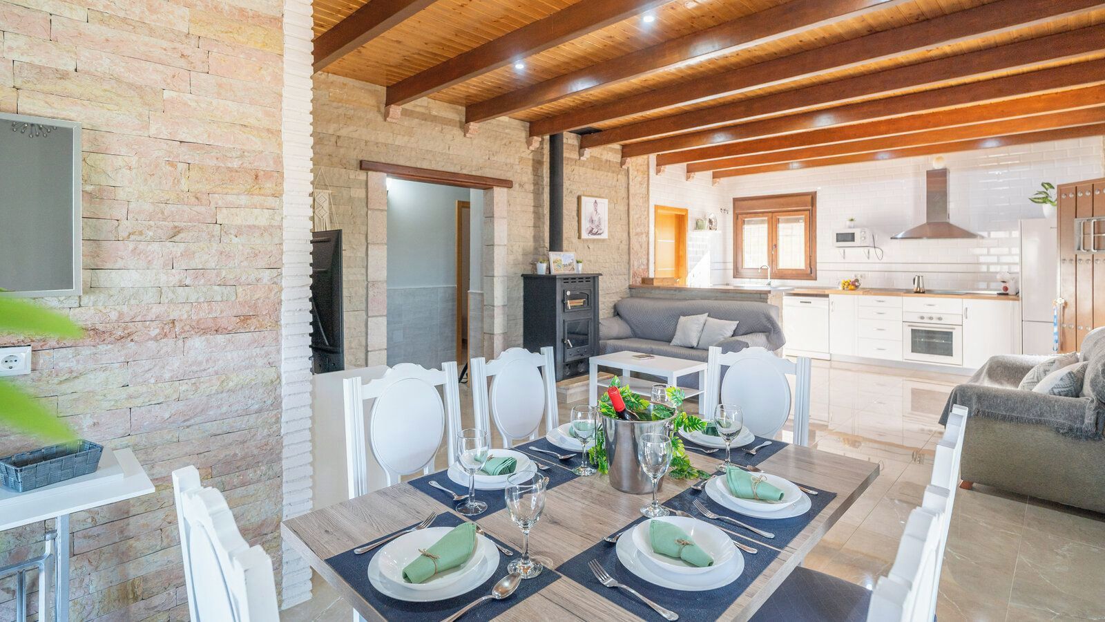 Un coin repas avec une table dressée pour quatre personnes, une cuisine en arrière-plan et un mur en pierre.